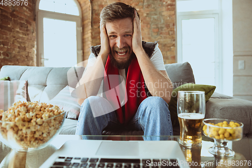 Image of Excited football fan watching sport match at home, remote support of favourite team during coronavirus pandemic outbreak