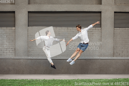 Image of Jumping young couple in front of buildings, on the run in jump high