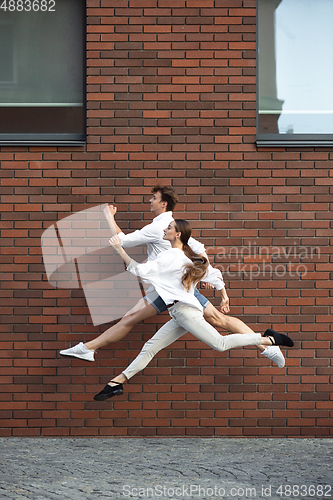 Image of Jumping young couple in front of buildings, on the run in jump high