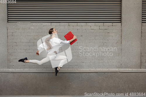 Image of Jumping young woman in front of buildings, on the run in jump high