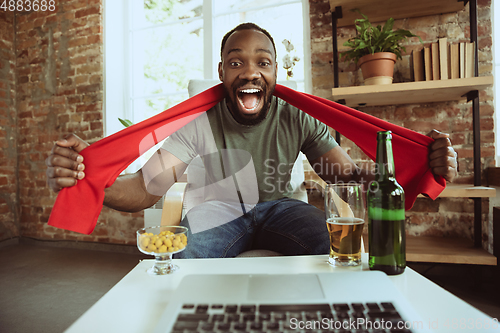 Image of Excited football fan watching sport match at home, remote support of favourite team during coronavirus pandemic outbreak