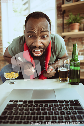 Image of Excited football fan watching sport match at home, remote support of favourite team during coronavirus pandemic outbreak