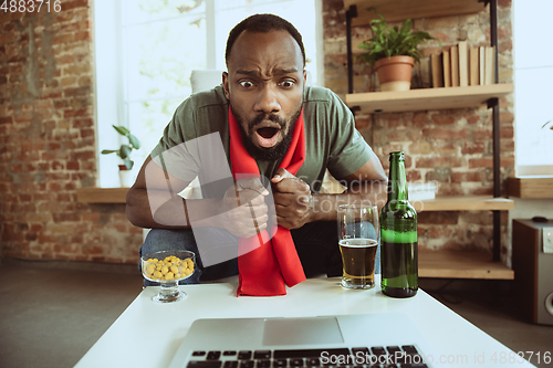 Image of Excited football fan watching sport match at home, remote support of favourite team during coronavirus pandemic outbreak