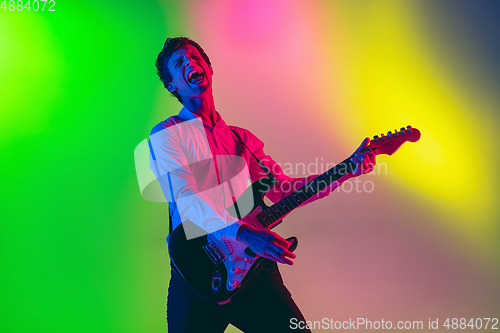 Image of Young caucasian musician, guitarist playing on gradient background in neon light. Concept of music, hobby, festival