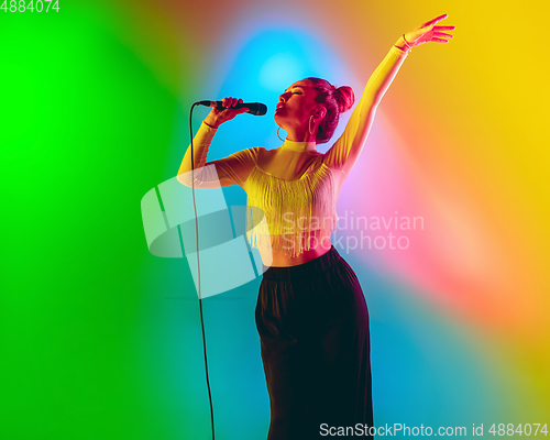 Image of Young caucasian musician playing, singing on gradient background in neon light. Concept of music, hobby, festival