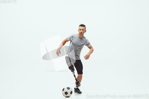 Image of Athlete with disabilities or amputee isolated on white studio background. Professional male football player with leg prosthesis training and practicing in studio.