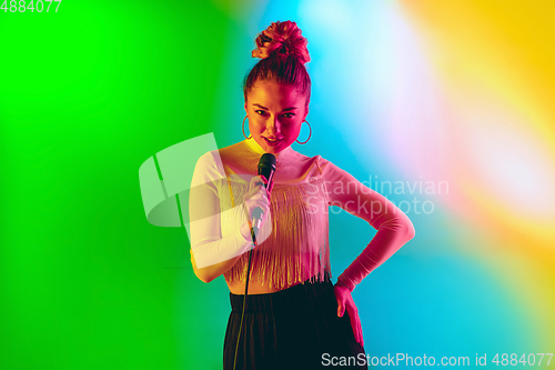 Image of Young caucasian musician playing, singing on gradient background in neon light. Concept of music, hobby, festival