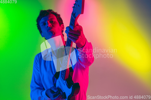 Image of Young caucasian musician, guitarist playing on gradient background in neon light. Concept of music, hobby, festival