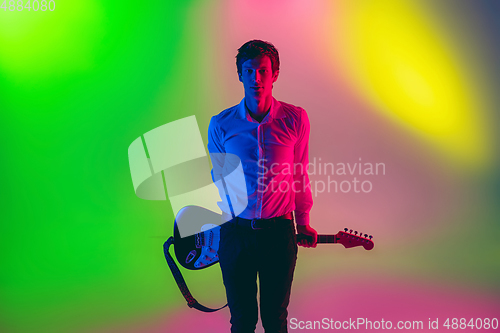 Image of Young caucasian musician, guitarist playing on gradient background in neon light. Concept of music, hobby, festival