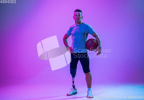 Image of Athlete with disabilities or amputee isolated on gradient studio background. Professional male basketball player with leg prosthesis training and practicing in studio.