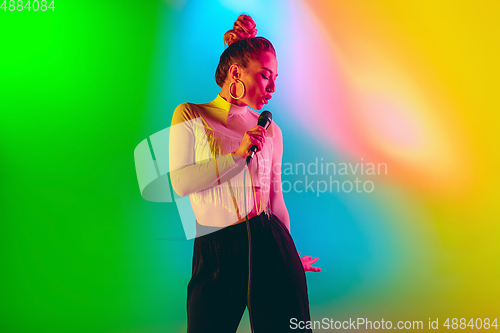 Image of Young caucasian musician playing, singing on gradient background in neon light. Concept of music, hobby, festival