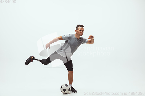 Image of Athlete with disabilities or amputee isolated on white studio background. Professional male football player with leg prosthesis training and practicing in studio.