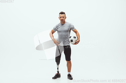 Image of Athlete with disabilities or amputee isolated on white studio background. Professional male football player with leg prosthesis training and practicing in studio.