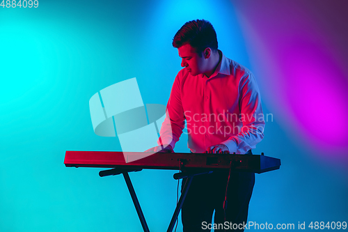 Image of Young caucasian musician, keyboardist playing on gradient background in neon light. Concept of music, hobby, festival
