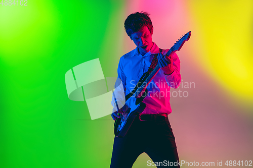 Image of Young caucasian musician, guitarist playing on gradient background in neon light. Concept of music, hobby, festival