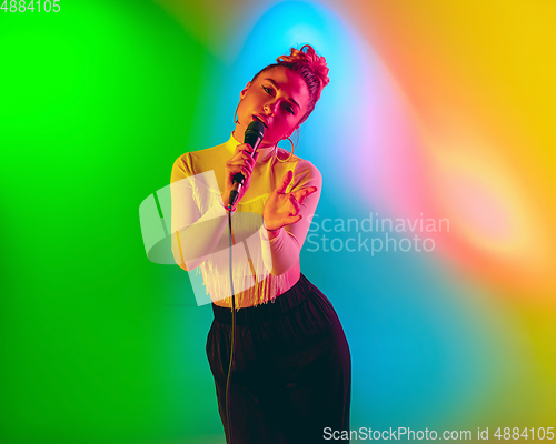 Image of Young caucasian musician playing, singing on gradient background in neon light. Concept of music, hobby, festival