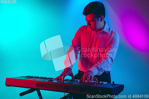 Image of Young caucasian musician, keyboardist playing on gradient background in neon light. Concept of music, hobby, festival