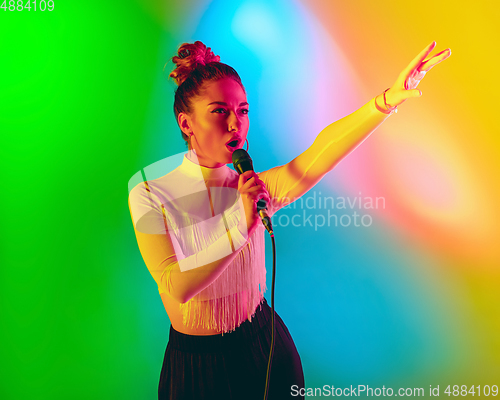 Image of Young caucasian musician playing, singing on gradient background in neon light. Concept of music, hobby, festival