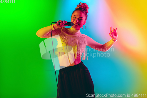 Image of Young caucasian musician playing, singing on gradient background in neon light. Concept of music, hobby, festival