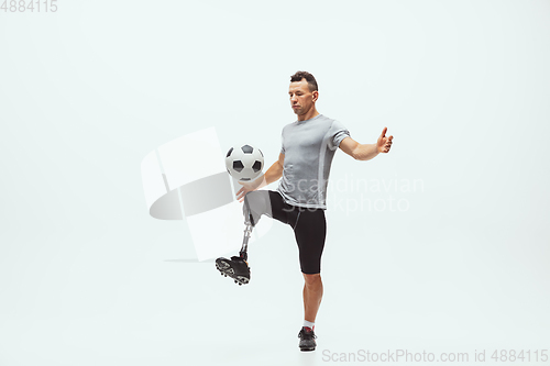 Image of Athlete with disabilities or amputee isolated on white studio background. Professional male football player with leg prosthesis training and practicing in studio.