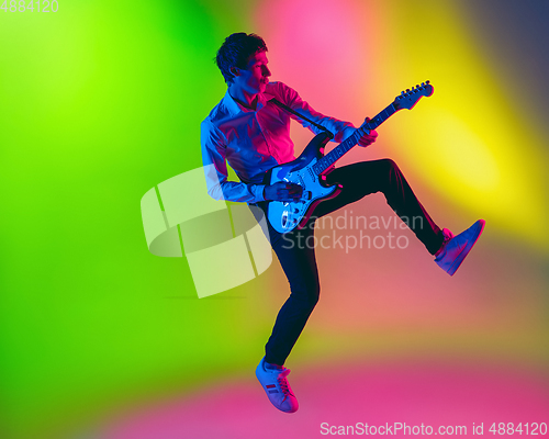 Image of Young caucasian musician, guitarist playing on gradient background in neon light. Concept of music, hobby, festival