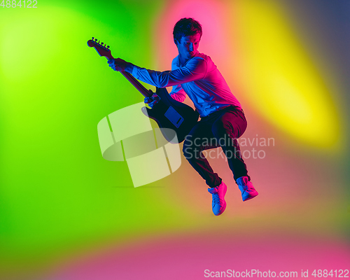 Image of Young caucasian musician, guitarist playing on gradient background in neon light. Concept of music, hobby, festival