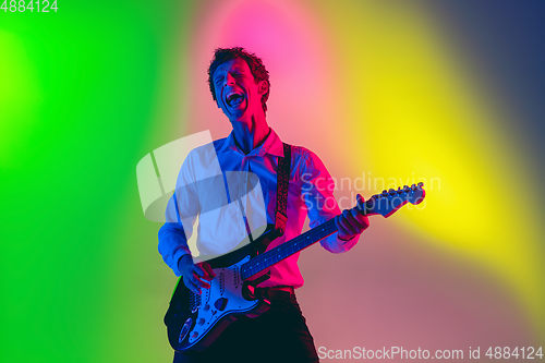 Image of Young caucasian musician, guitarist playing on gradient background in neon light. Concept of music, hobby, festival