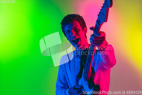 Image of Young caucasian musician, guitarist playing on gradient background in neon light. Concept of music, hobby, festival