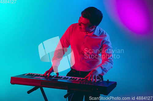 Image of Young caucasian musician, keyboardist playing on gradient background in neon light. Concept of music, hobby, festival