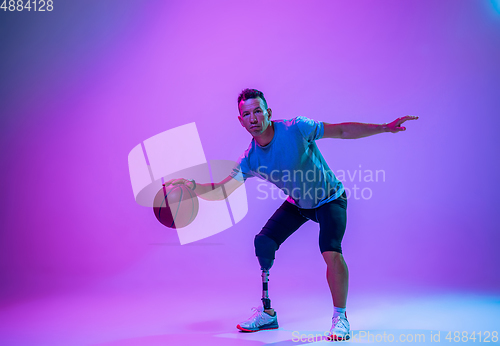 Image of Athlete with disabilities or amputee isolated on gradient studio background. Professional male basketball player with leg prosthesis training and practicing in studio.