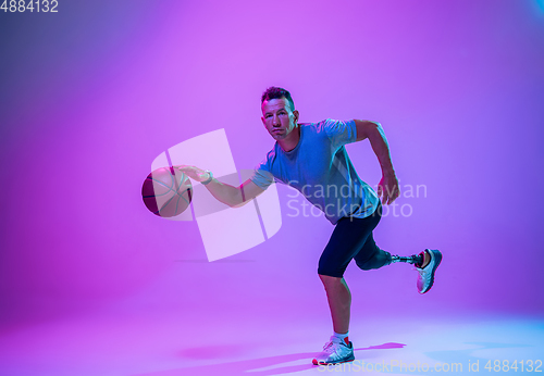 Image of Athlete with disabilities or amputee isolated on gradient studio background. Professional male basketball player with leg prosthesis training and practicing in studio.