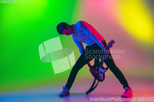 Image of Young caucasian musician, guitarist playing on gradient background in neon light. Concept of music, hobby, festival