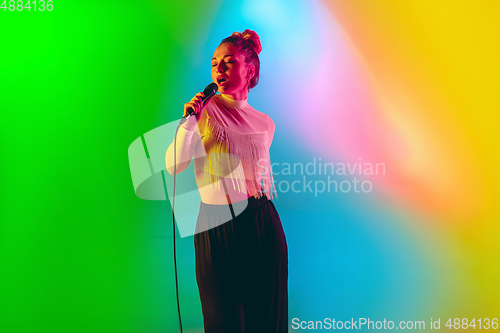 Image of Young caucasian musician playing, singing on gradient background in neon light. Concept of music, hobby, festival