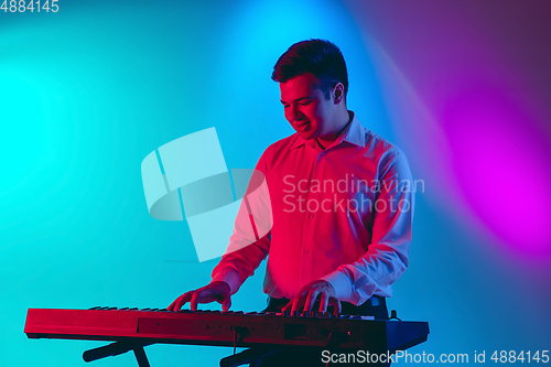 Image of Young caucasian musician, keyboardist playing on gradient background in neon light. Concept of music, hobby, festival