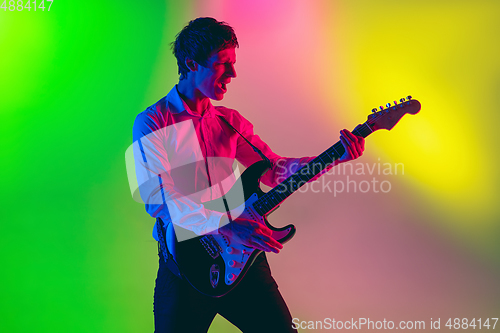 Image of Young caucasian musician, guitarist playing on gradient background in neon light. Concept of music, hobby, festival