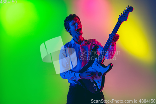 Image of Young caucasian musician, guitarist playing on gradient background in neon light. Concept of music, hobby, festival