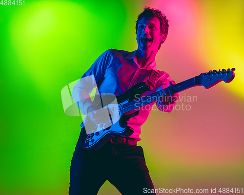Image of Young caucasian musician, guitarist playing on gradient background in neon light. Concept of music, hobby, festival