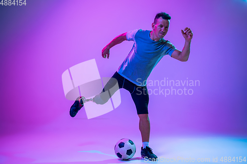 Image of Athlete with disabilities or amputee isolated on gradient studio background. Professional male football player with leg prosthesis training and practicing in studio.