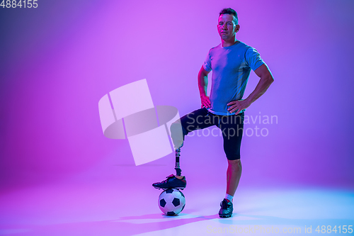 Image of Athlete with disabilities or amputee isolated on gradient studio background. Professional male football player with leg prosthesis training and practicing in studio.