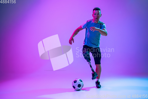Image of Athlete with disabilities or amputee isolated on gradient studio background. Professional male football player with leg prosthesis training and practicing in studio.