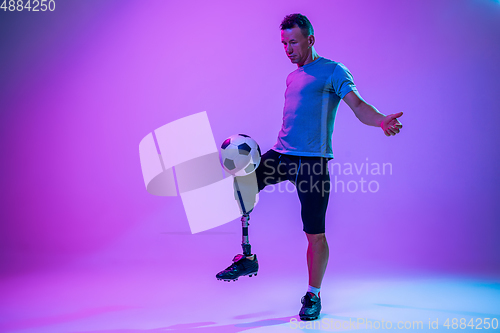 Image of Athlete with disabilities or amputee isolated on gradient studio background. Professional male football player with leg prosthesis training and practicing in studio.