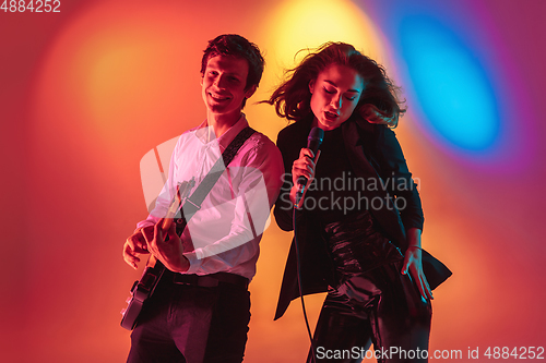 Image of Young caucasian musicians, female singer and guitarist performing on gradient background in neon light. Concept of music, hobby, festival