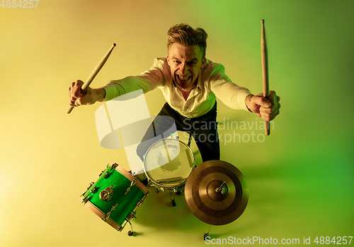 Image of Young caucasian musician, drummer playing on gradient background in neon light. Concept of music, hobby, festival