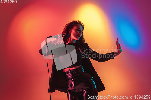 Image of Young caucasian musician, female singer performing on gradient background in neon light. Concept of music, hobby, festival