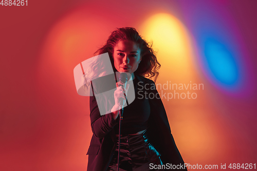 Image of Young caucasian musician, female singer performing on gradient background in neon light. Concept of music, hobby, festival