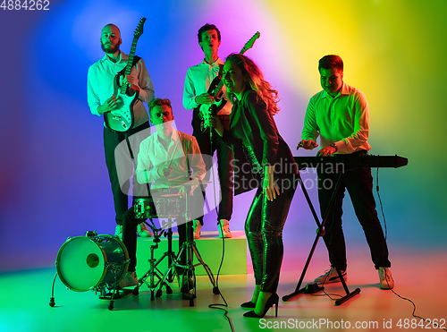 Image of Young caucasian musicians, band playing on gradient background in neon light. Concept of music, hobby, festival