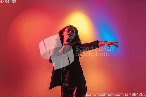 Image of Young caucasian musician, female singer performing on gradient background in neon light. Concept of music, hobby, festival