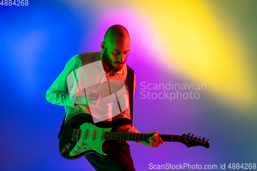 Image of Young caucasian musician, guitarist playing on gradient background in neon light. Concept of music, hobby, festival
