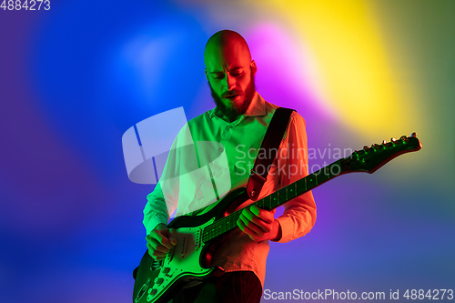 Image of Young caucasian musician, guitarist playing on gradient background in neon light. Concept of music, hobby, festival