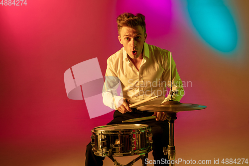 Image of Young caucasian musician, drummer playing on gradient background in neon light. Concept of music, hobby, festival